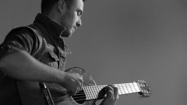 -白黒灰色の壁の背景に座ってアコースティック ギターで演奏するギタリスト — ストック動画