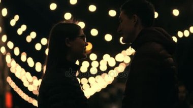Genç çift siluet bir gecede sokak, garland arka plan öp.