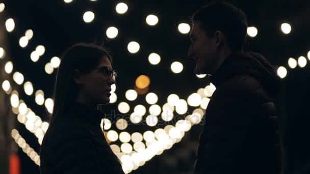 若いカップルが夜の街中、ガーランドの背景にシルエットをキスします。 — ストック動画