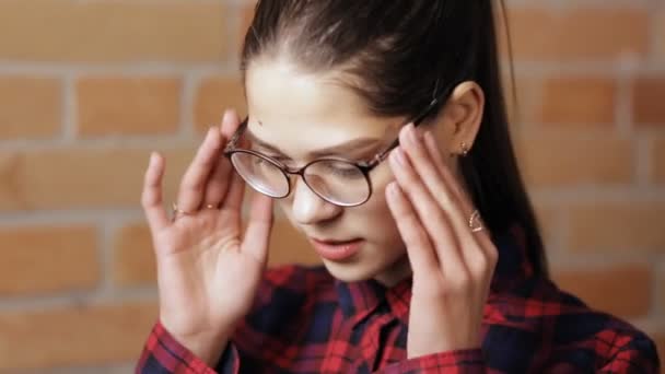 Primer plano de la atractiva mujer con gafas en el fondo de la pared de ladrillo — Vídeos de Stock