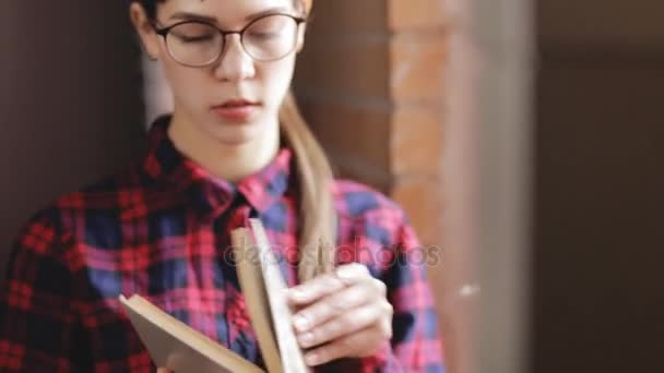Ελκυστική γυναίκα σε γυαλιά ανάγνωσης βιβλίου στέκεται στο παράθυρο — Αρχείο Βίντεο