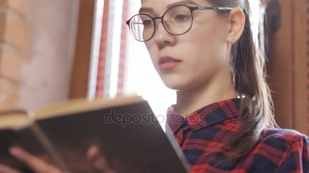 Привлекательная женщина в очках читает книгу, стоя у окна — стоковое видео