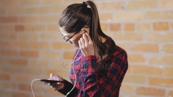 Mujer joven escuchando música y bailando en el fondo de la pared de ladrillo — Vídeos de Stock