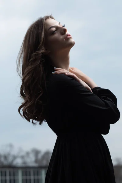Vakker kvinne i svart kjole mot sur himmelbakgrunn – stockfoto