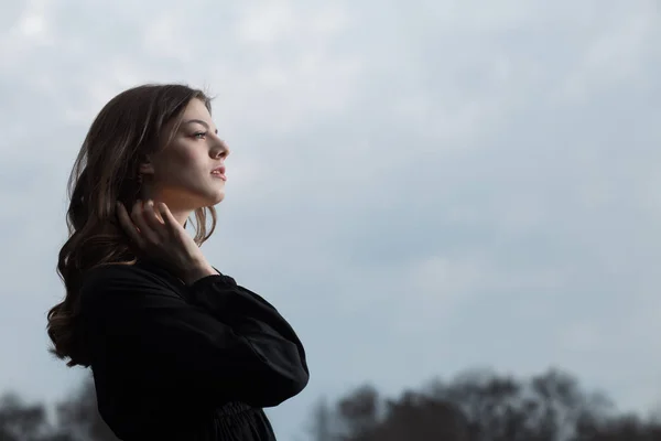 Hermosa mujer en vestido negro contra el fondo del cielo sombrío —  Fotos de Stock