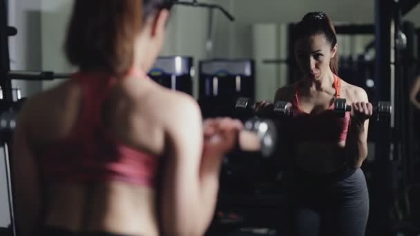 Deporte mujer levantando mancuerna en el gimnasio, bíceps ejercicio en el espejo — Vídeo de stock