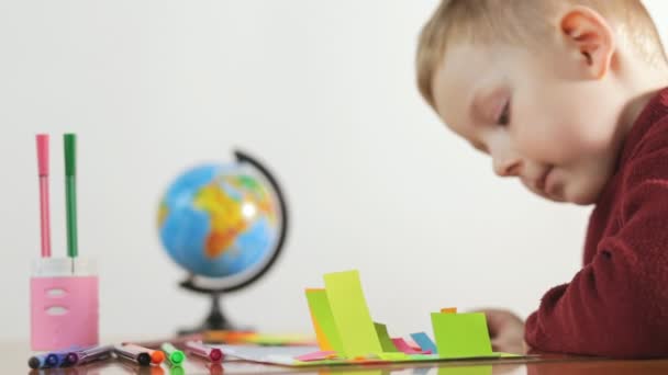 Little boy draws a markers on color paper, white background. — Stock Video