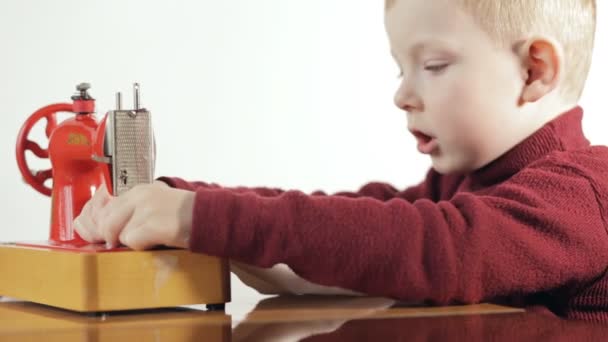 Маленький хлопчик шиє тканину на швейній машинці - білий фон — стокове відео