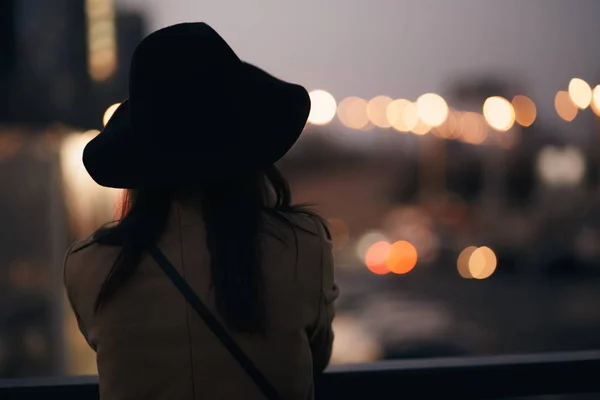 Menina silhueta em chapéu olhando para a cidade da noite — Fotografia de Stock