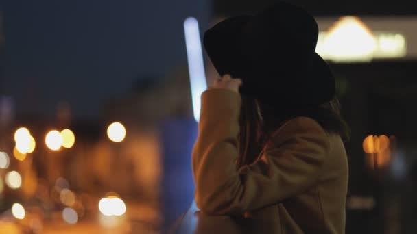 Mujer en sombrero en la noche mirando al paisaje urbano — Vídeos de Stock