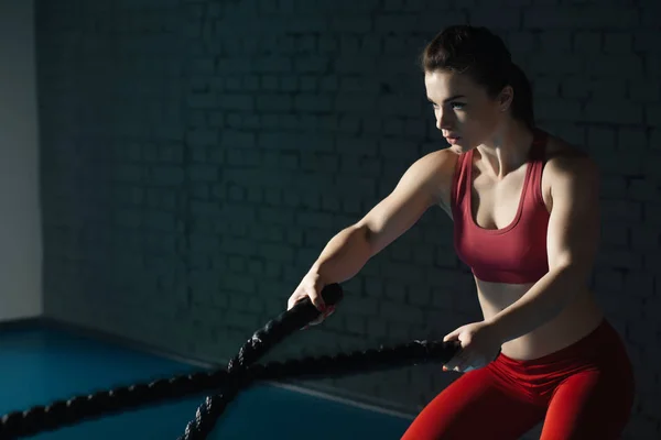 Strong woman with battle rope in gym