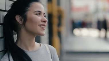 Bir kameraya bakarak tuğla duvar yakınındaki şehirde gülümseyen kadın