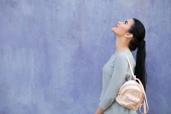 Stylische Frau mit Tasche an der violetten Wand — Stockfoto