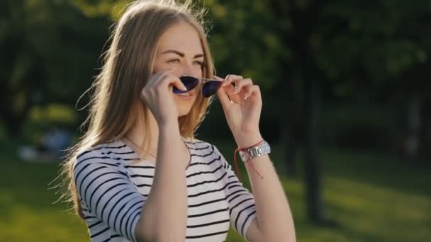 Девочка-подросток одевает солнечные очки в парке — стоковое видео