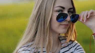 Güneş gözlüğü ve kamera göz kırpmalara çimenlerin üzerinde oturan kız