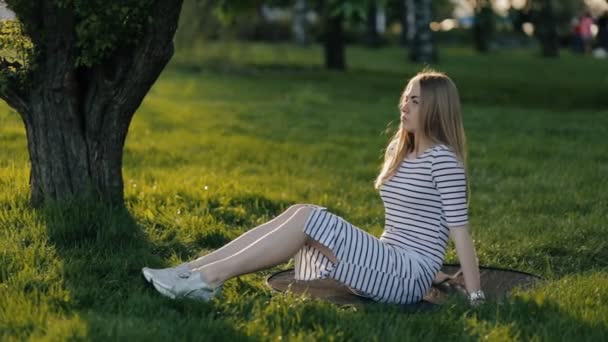 Çimenlerin üzerinde oturan ve rahatlatıcı yorgun genç kız — Stok video
