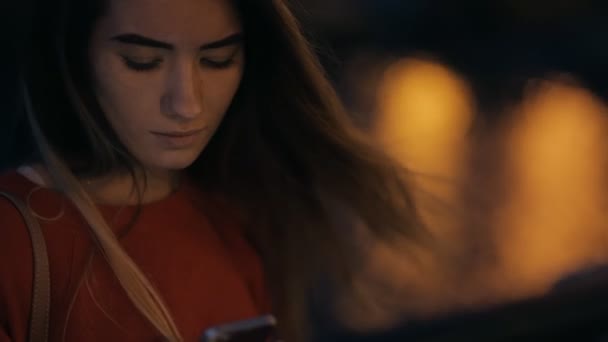Νεαρή γυναίκα κοιτάζοντας προς τα κάτω της έξυπνο τηλέφωνο το βράδυ — Αρχείο Βίντεο