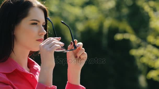 Portrét sluneční brýle dresinkem hezká žena v parku — Stock video