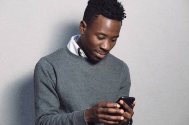 Afrika kökenli Amerikalı adam cep telefonuyla gri duvarının yakınında