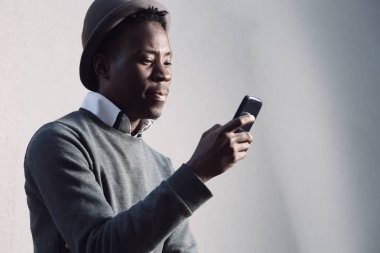 Afrika kökenli Amerikalı adam cep telefonuyla gri duvarının yakınında