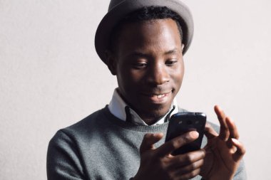 Afrika kökenli Amerikalı adam cep telefonuyla gri duvarının yakınında