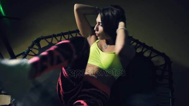 Pretty sports woman pumping press muscle on rebounder in dark gym — Stock Footage Pretty sports woman pumping press muscle on rebounder in dark gym Video Clip
