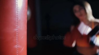 Genç kadın boks kum torbası karanlık bir salonda