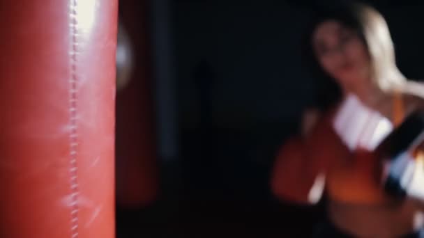 Молодая женщина боксирует боксерскую грушу в темном зале — стоковое видео