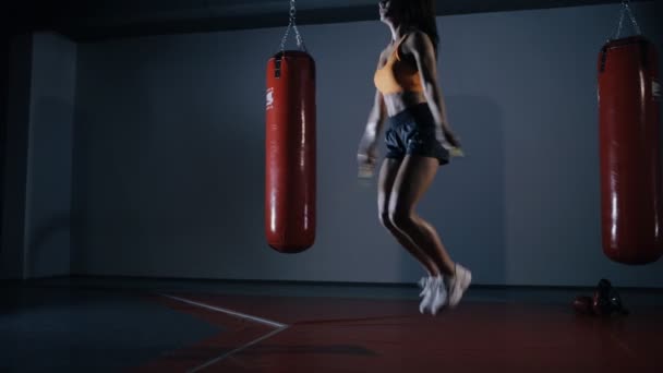 Mulher jovem boxeador pulando em uma corda pulando em um salão escuro — Vídeo de Stock
