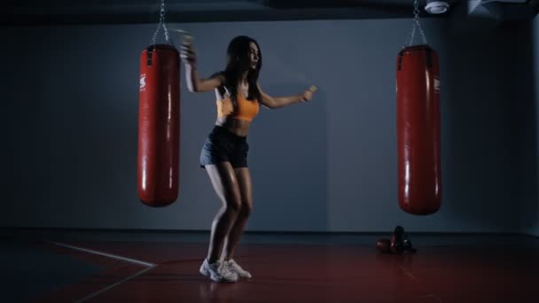 Young woman boxer jumping on a skipping rope in a dark hall — Stock Video