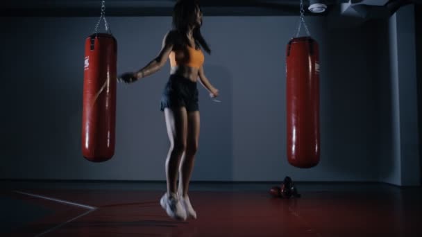 Mujer joven boxeadora saltando en una cuerda en un pasillo oscuro — Vídeo de stock