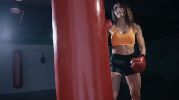 Молодая женщина боксирует боксерскую грушу в темном зале — стоковое видео