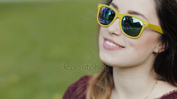 Portrait of young woman sitting on grass in sunglasses — Stock Video