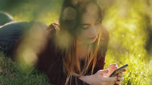 Schöne Frau im Gras liegend und Smartphone benutzend — Stockvideo