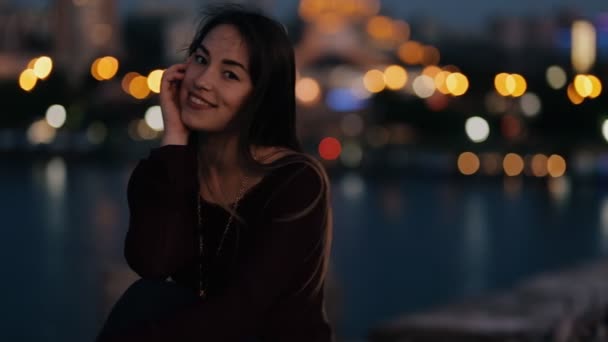 Mulher bonita sentada em uma ponte à noite e relaxar — Vídeo de Stock
