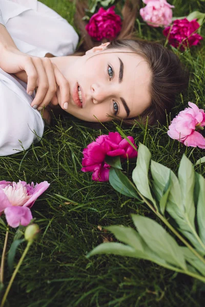 Woman lying on grass with flowers peonies around — Stock Photo, Image