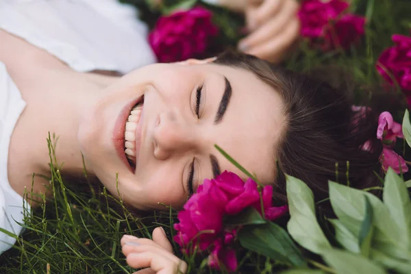 Женщина лежит на траве с цветами пионы вокруг — стоковое фото
