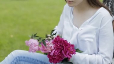 Kadın parkta çim üzerinde oturan peonies buket yapar
