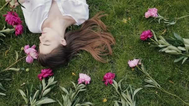 Vrouw liggen op gras met bloemen pioenrozen rond — Stockvideo