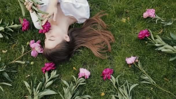 Vrouw liggen op gras met bloemen pioenrozen rond — Stockvideo