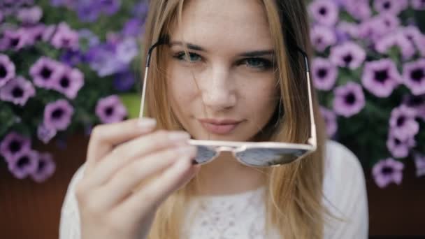 Hübsche Frau sitzt neben Blumen und trägt Sonnenbrille in der Stadt, Zeitlupe — Stockvideo