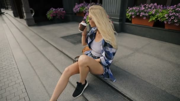 Женщина пьет кофе сидя на городской улице — стоковое видео