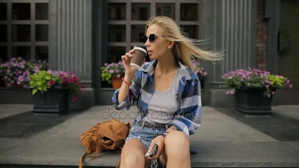 Женщина пьет кофе сидя на городской улице — стоковое видео