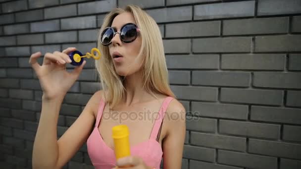 Mujer feliz soplando burbujas en la pared de ladrillo en cámara lenta — Vídeos de Stock