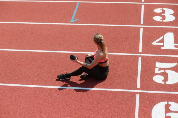 Young sporty woman athlete in sportswear sitting and keep shake with water on stadium track