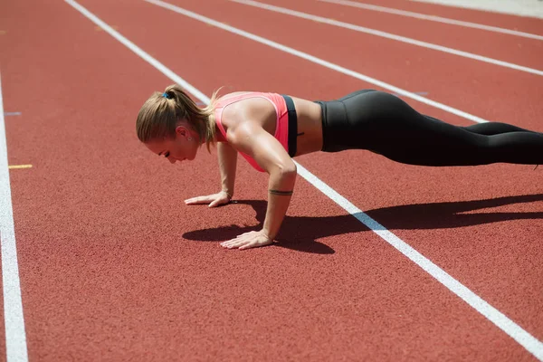 Young sporty woman athlete in sportswear push ups on stadium track, outdoor workout — Stock Photo, Image