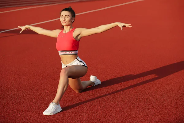 Giovane donna fitness carino. Attraente ragazza sportiva si allunga e si riscalda prima dell'allenamento nello stadio rosso, concetto di stile di vita sano. Praticare posa yoga . — Foto Stock