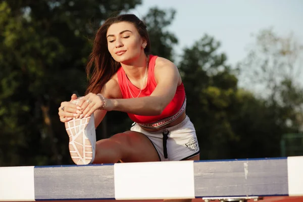 Joven atractivo fitness femenino. Mujer deportiva se estira y se calienta antes de entrenar en el estadio al aire libre en la barrera, concepto de estilo de vida saludable . — Foto de Stock