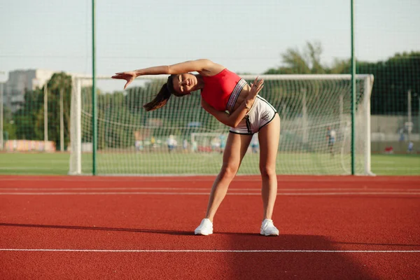 Giovane donna fitness carino. Attraente ragazza sportiva si allunga e si riscalda prima dell'allenamento nello stadio, concetto di stile di vita sano . — Foto Stock