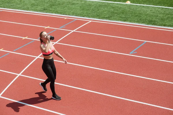 Joven atleta deportiva en ropa deportiva de agua potable o cóctel de proteínas de agitar en pista de estadio, concepto de entrenamiento — Foto de Stock